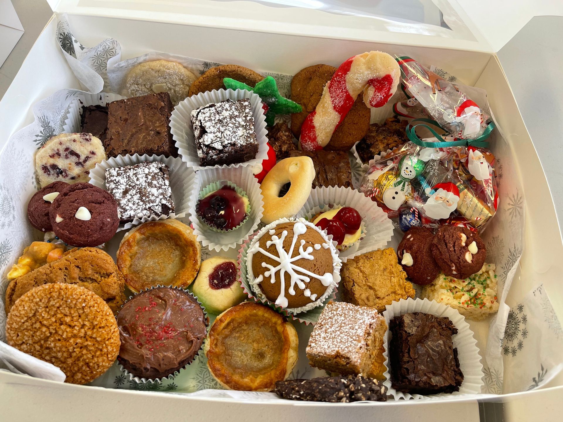 Assorted decorated holiday cookies in an open white box, including round, square, and ring-shaped treats