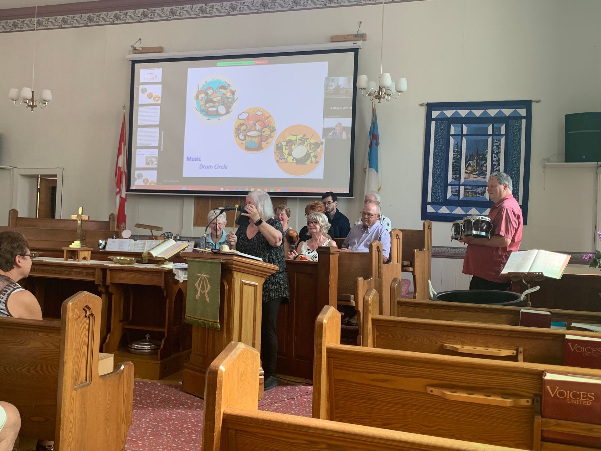 Speaker at a podium addresses a small group in a church hall with projected slides and pews.