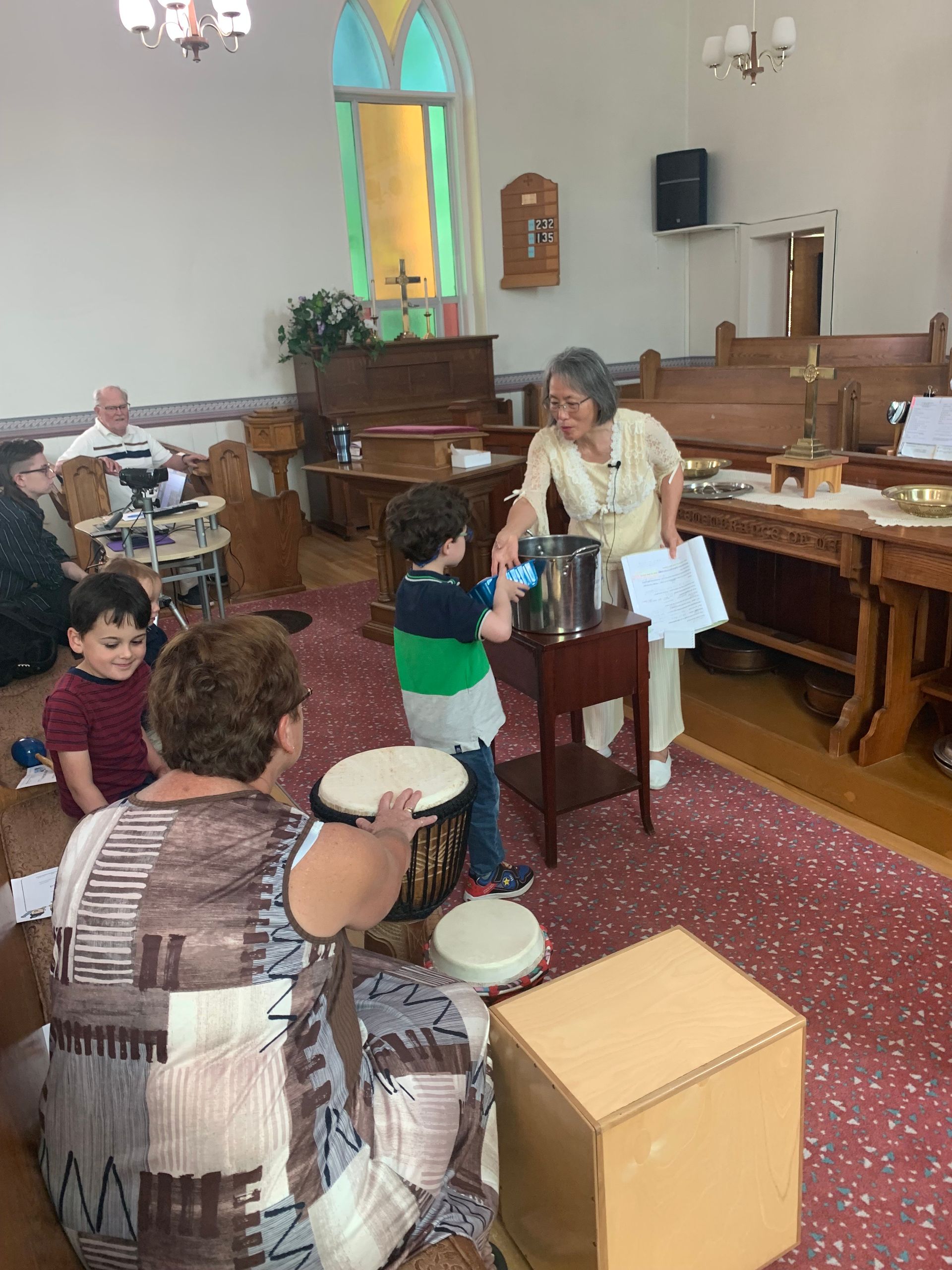 Children playing music in a church, with drums and a standing mic near the altar.