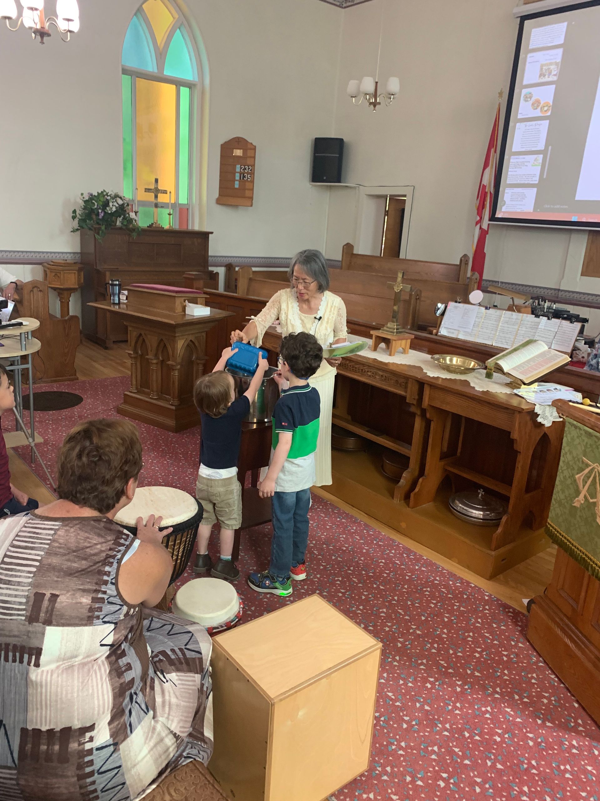 Two children with an adult in a church, near a drum and piano, with stained glass windows.