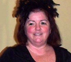 Smiling person with dark hair wearing a black top against a plain beige background