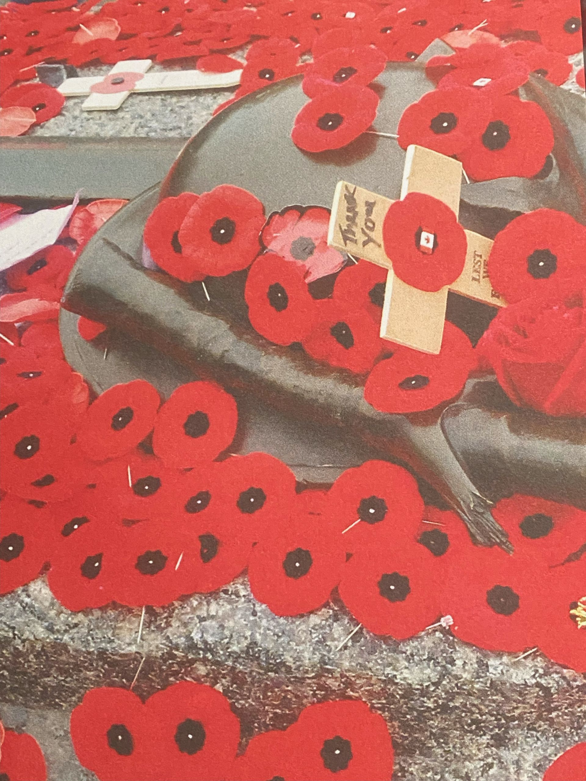 Red poppy wreaths and small wooden crosses on a gray memorial stone.