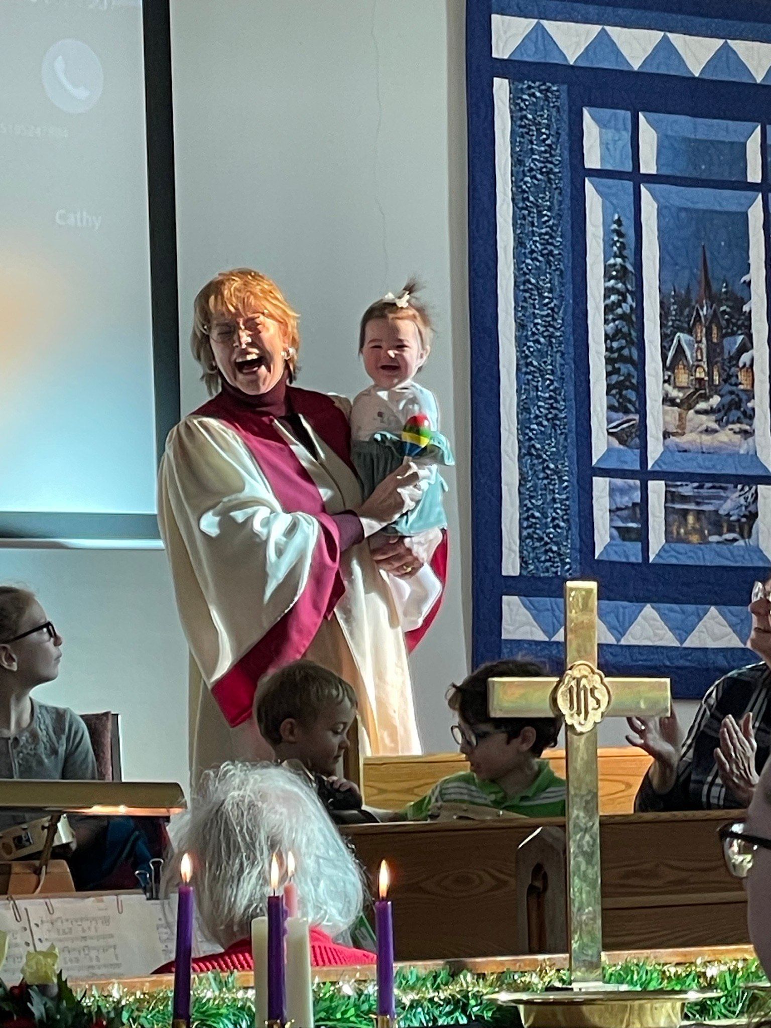 Woman holding a toddler beside a church altar with candles and a blue stained-glass backdrop