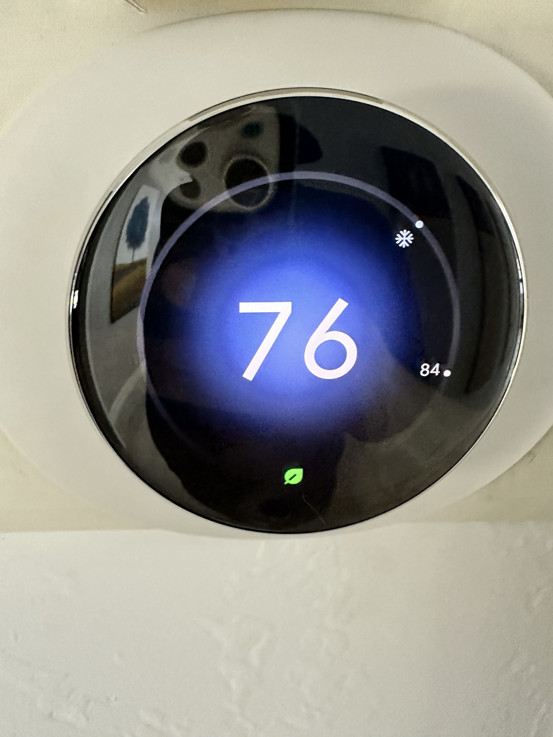 Round thermostat displaying 76°F with a blue-lit screen on a white wall