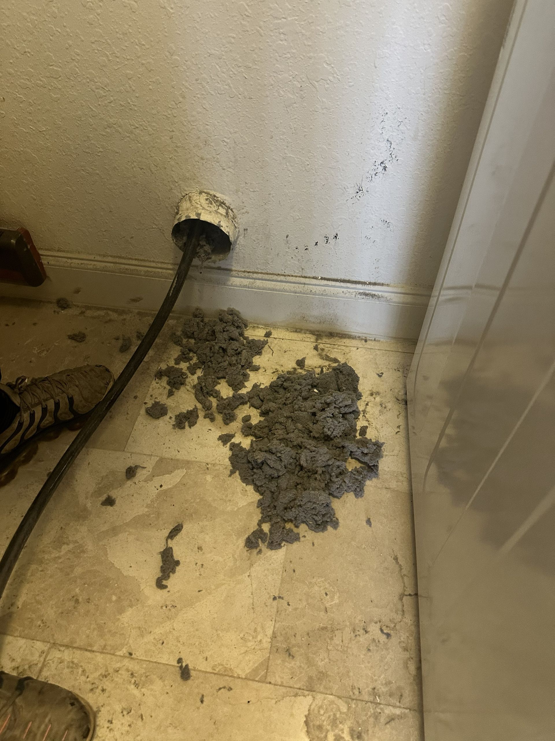 Bathroom floor with a pile of gray debris beneath a wall outlet and black cable.