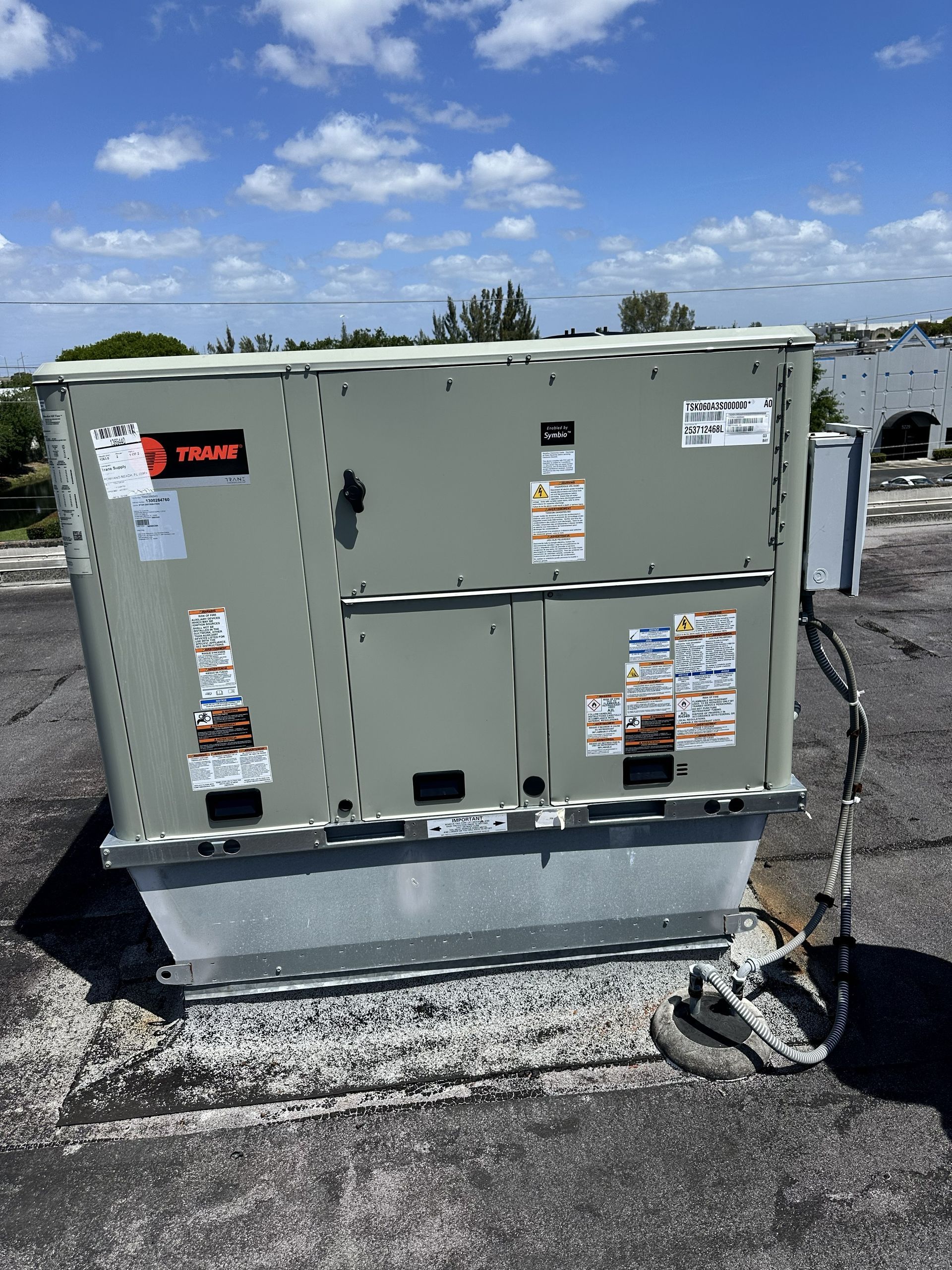 Gray rooftop HVAC unit with warning labels on a gravel-covered roof under a blue sky