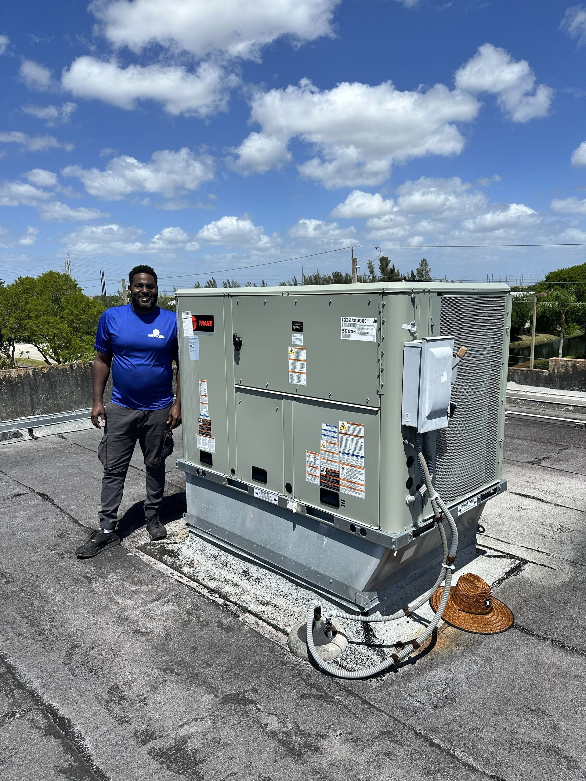 Man standing beside large rooftop HVAC unit under a partly cloudy sky