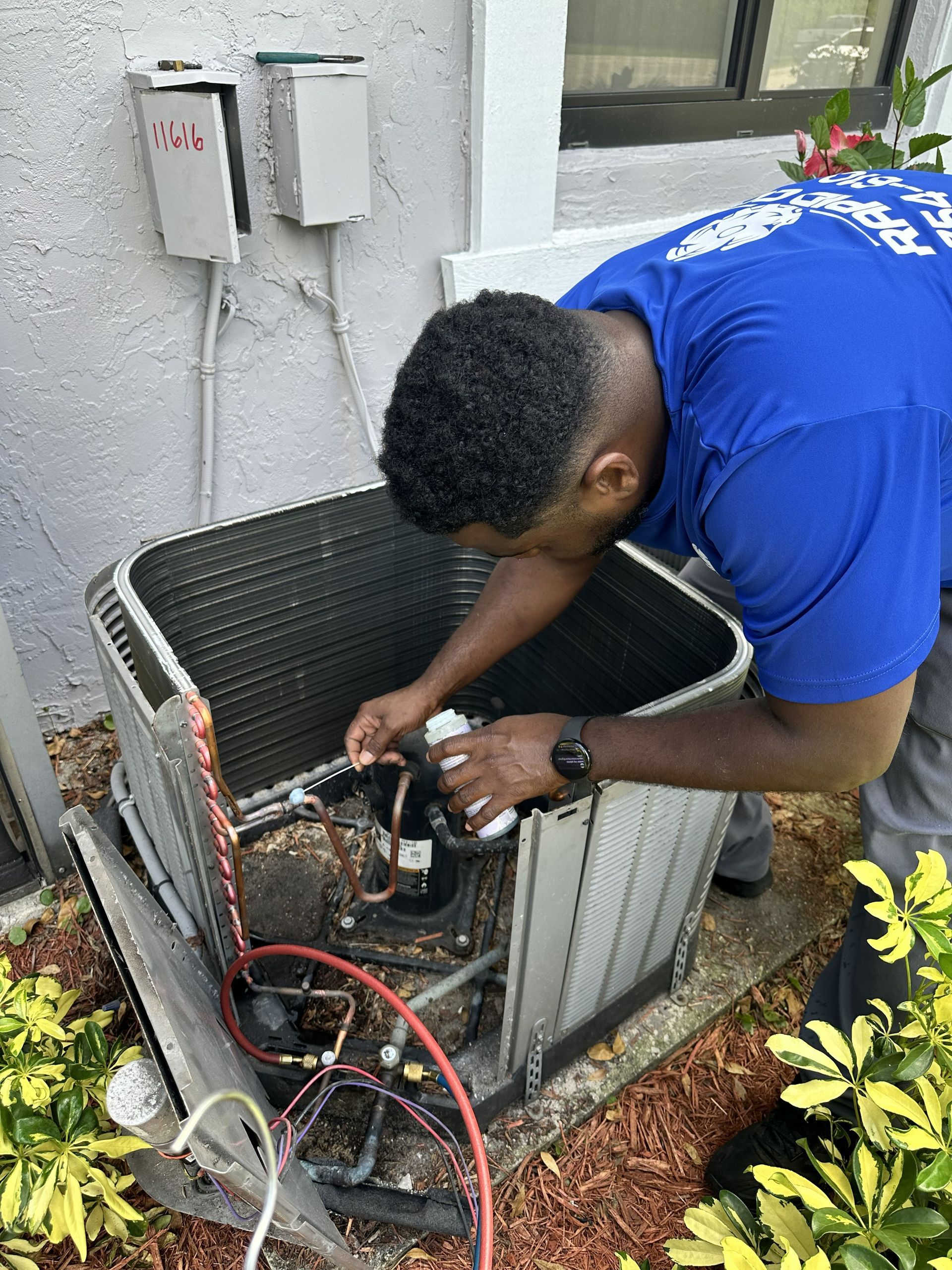 Technician in blue shirt inspecting an outdoor HVAC unit beside a building