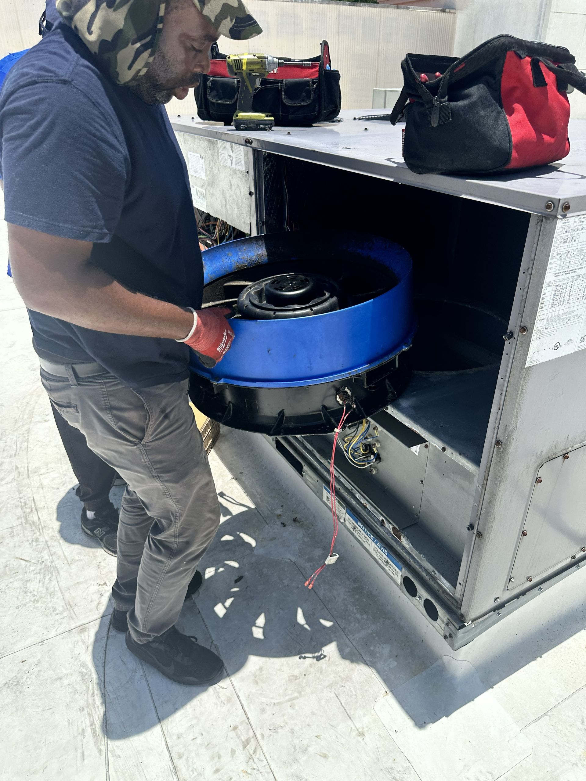 Worker installing a blue circular fan inside a metal rooftop HVAC unit
