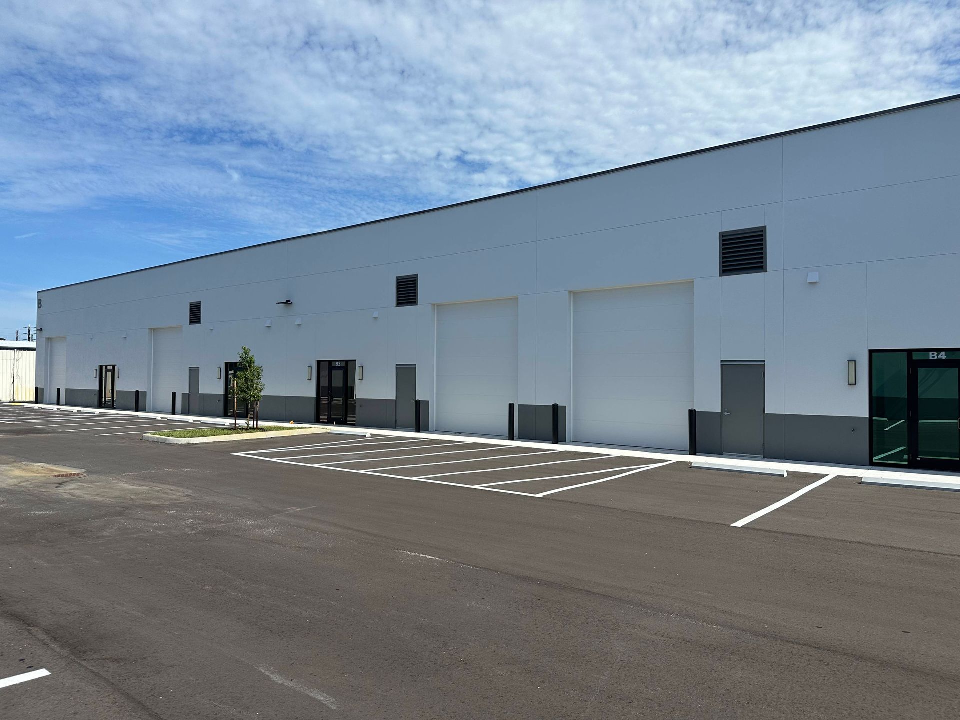 Large white industrial building beside an empty paved parking lot under a blue sky
