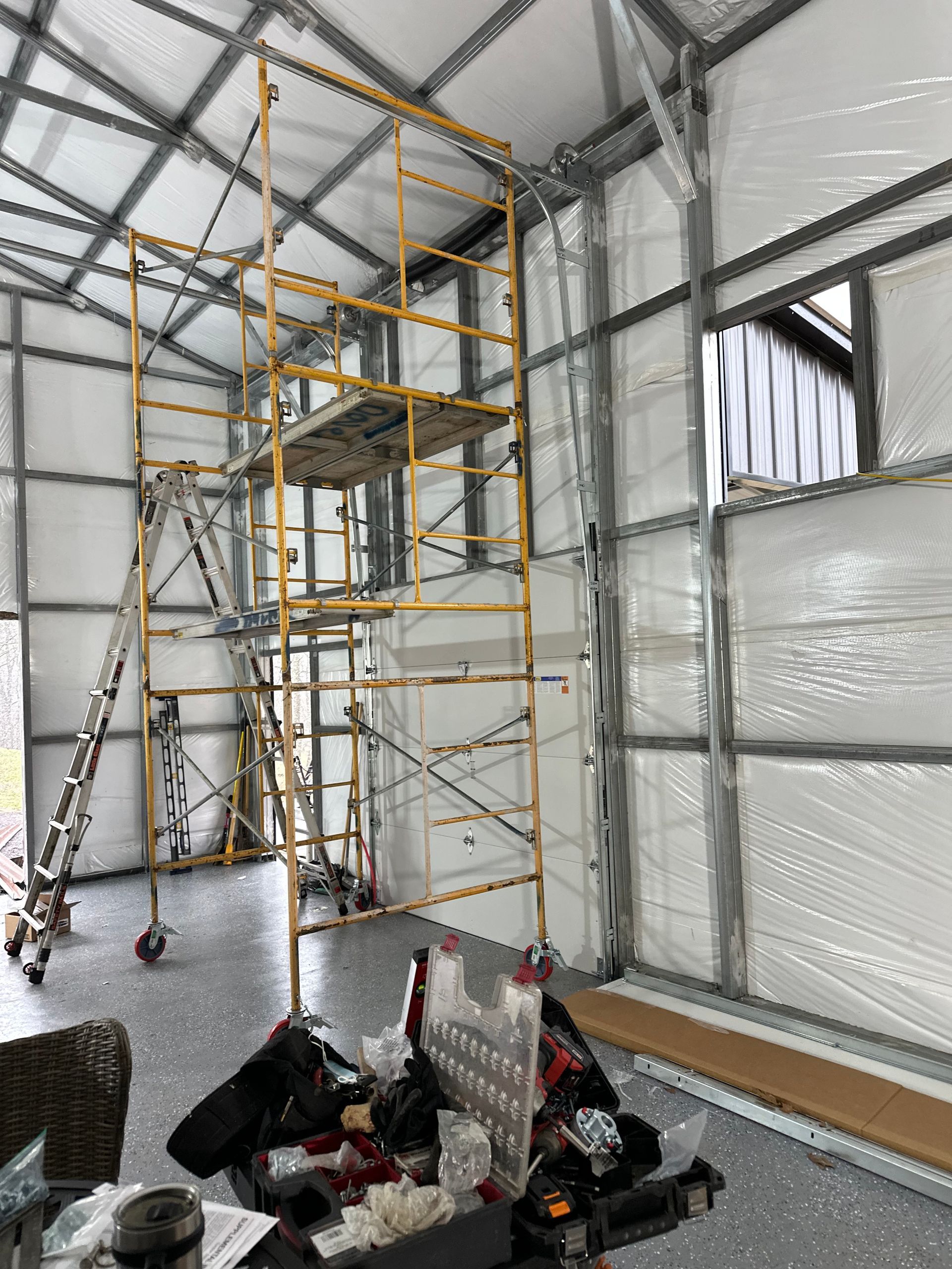 Scaffold tower inside a white-walled room with construction tools and materials on the floor.