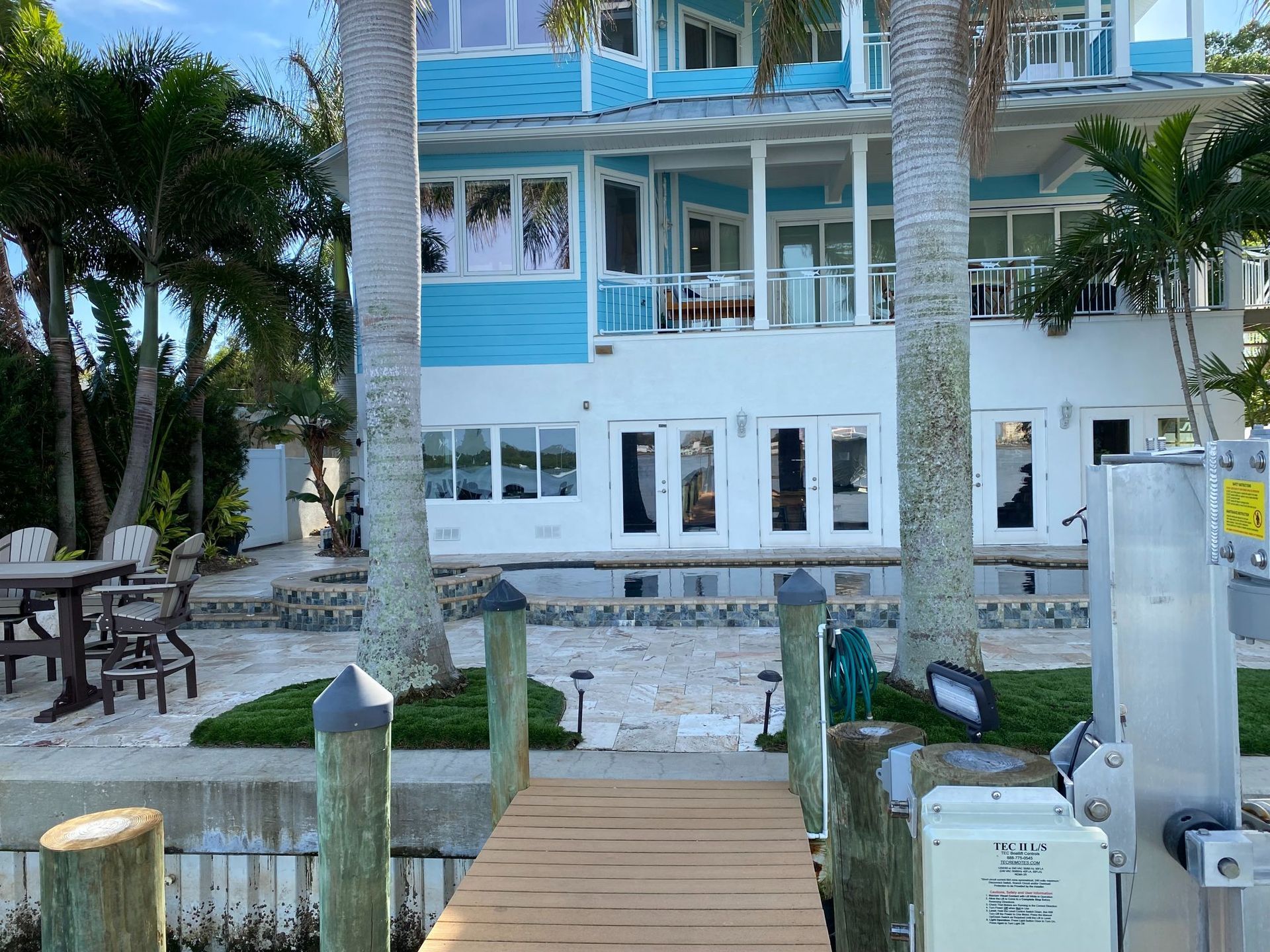 A multi-story, light blue house on the water, with a wooden dock in the foreground.