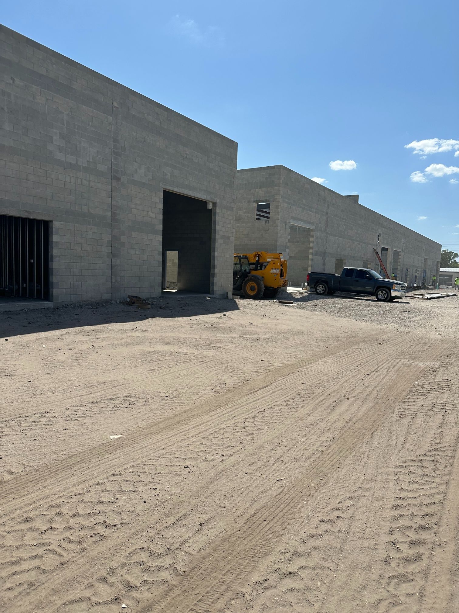 Construction site with concrete buildings, dirt ground, and equipment under a blue sky.