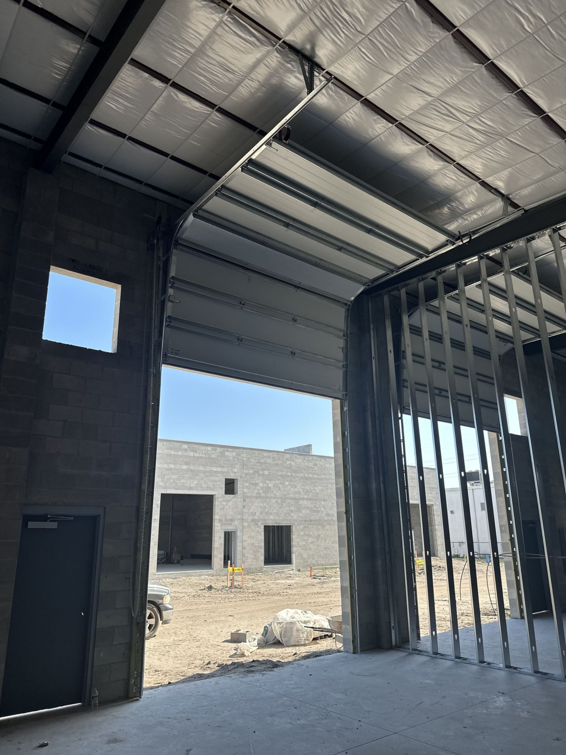 Interior of a building under construction, metal framing and a partially visible exterior, cloudy sky.