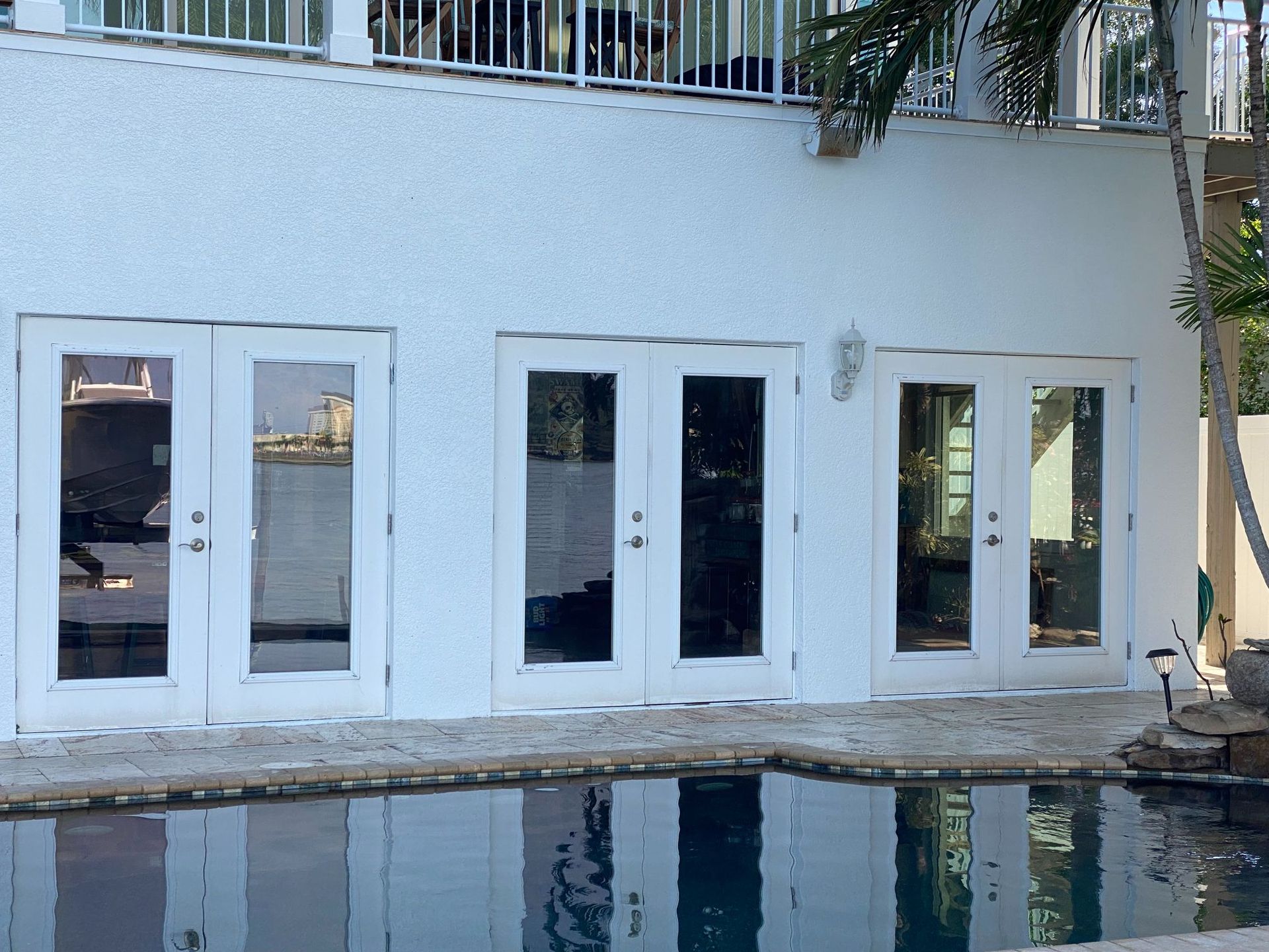 White house with glass doors overlooking a pool. Reflective water, sunny day.