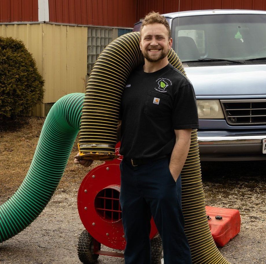 A man in a black shirt is standing next to a large green hose used for air duct cleaning