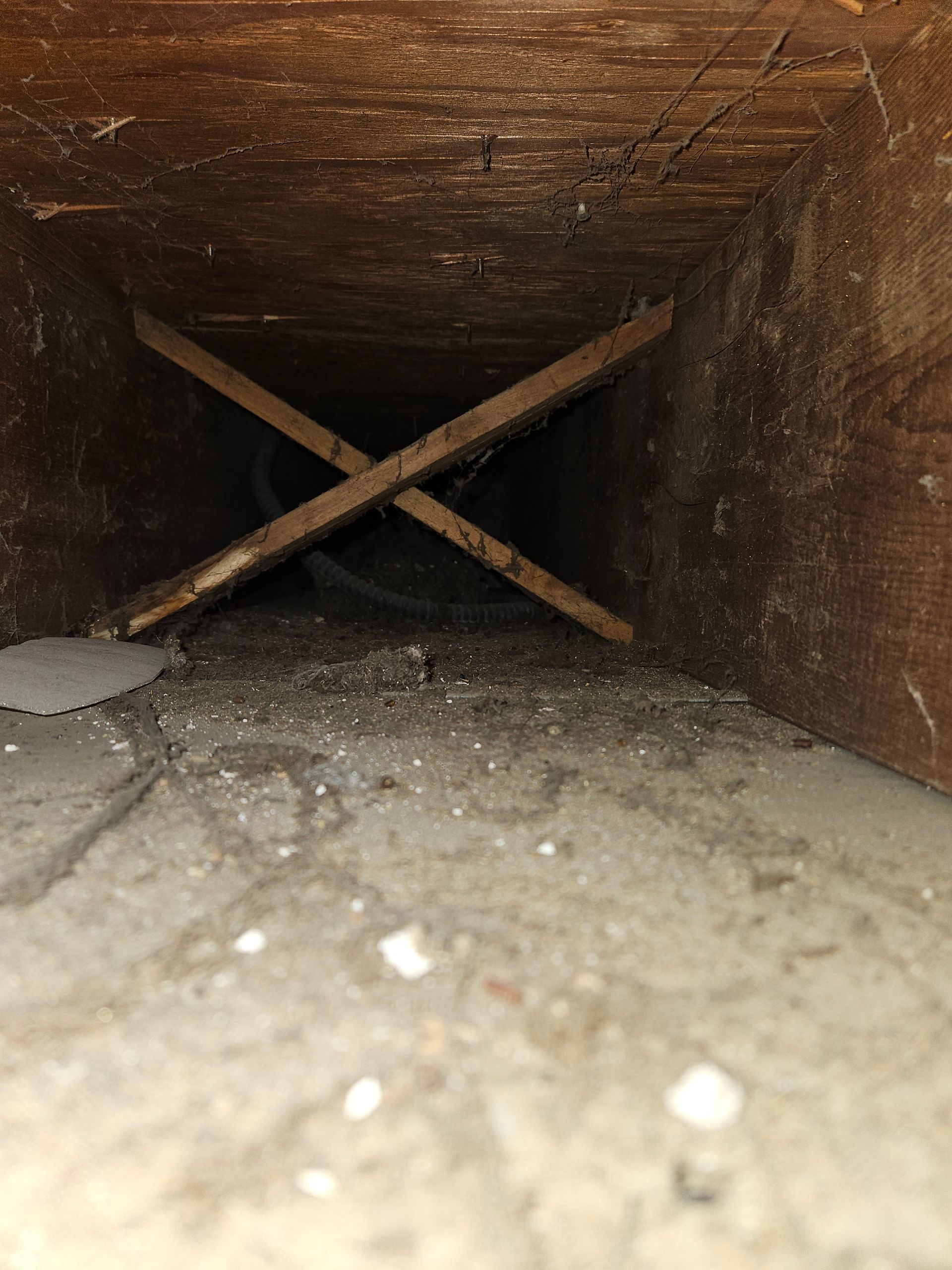 Wooden duct interior with crossed support beams. Dust and debris on the floor and walls.