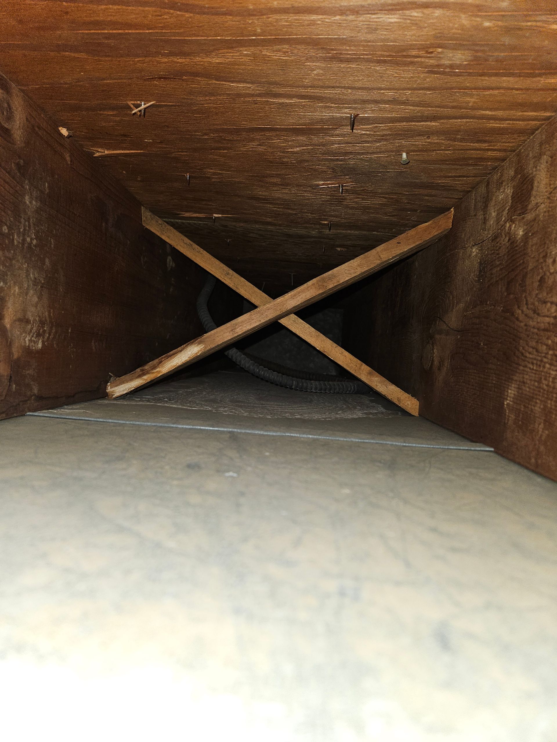 Wooden duct interior with X-shaped supports, a visible cable, and a gray floor.