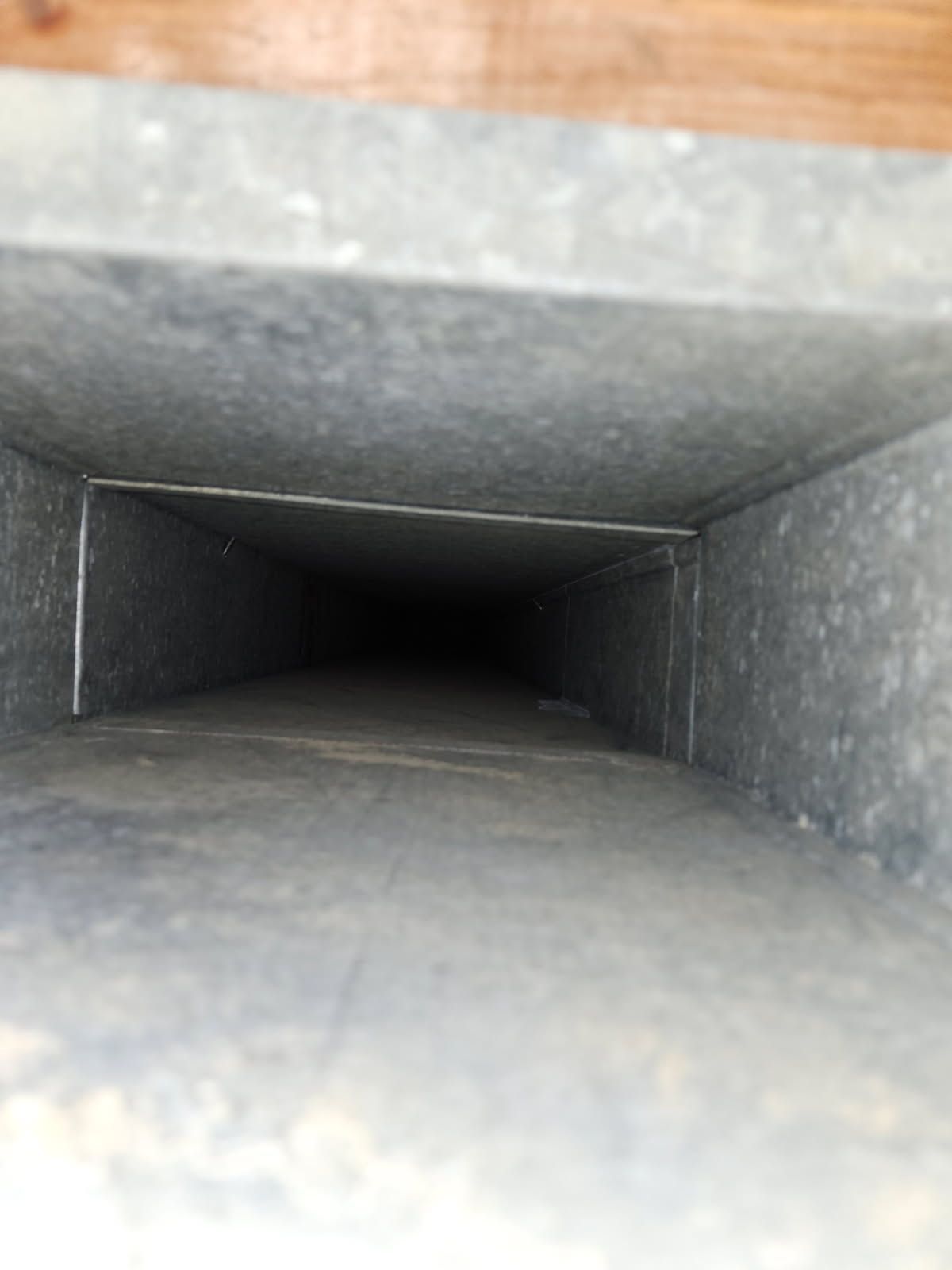 Interior view of a rectangular, metal air duct, empty and leading into darkness.