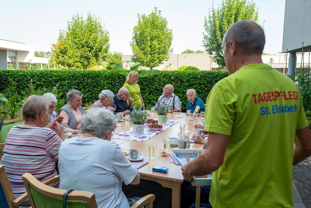 Gäste der Tagespflege Bühl sitzen zum Nachmittagskaffee im Garten und werden von Betreuungskräften bedient.