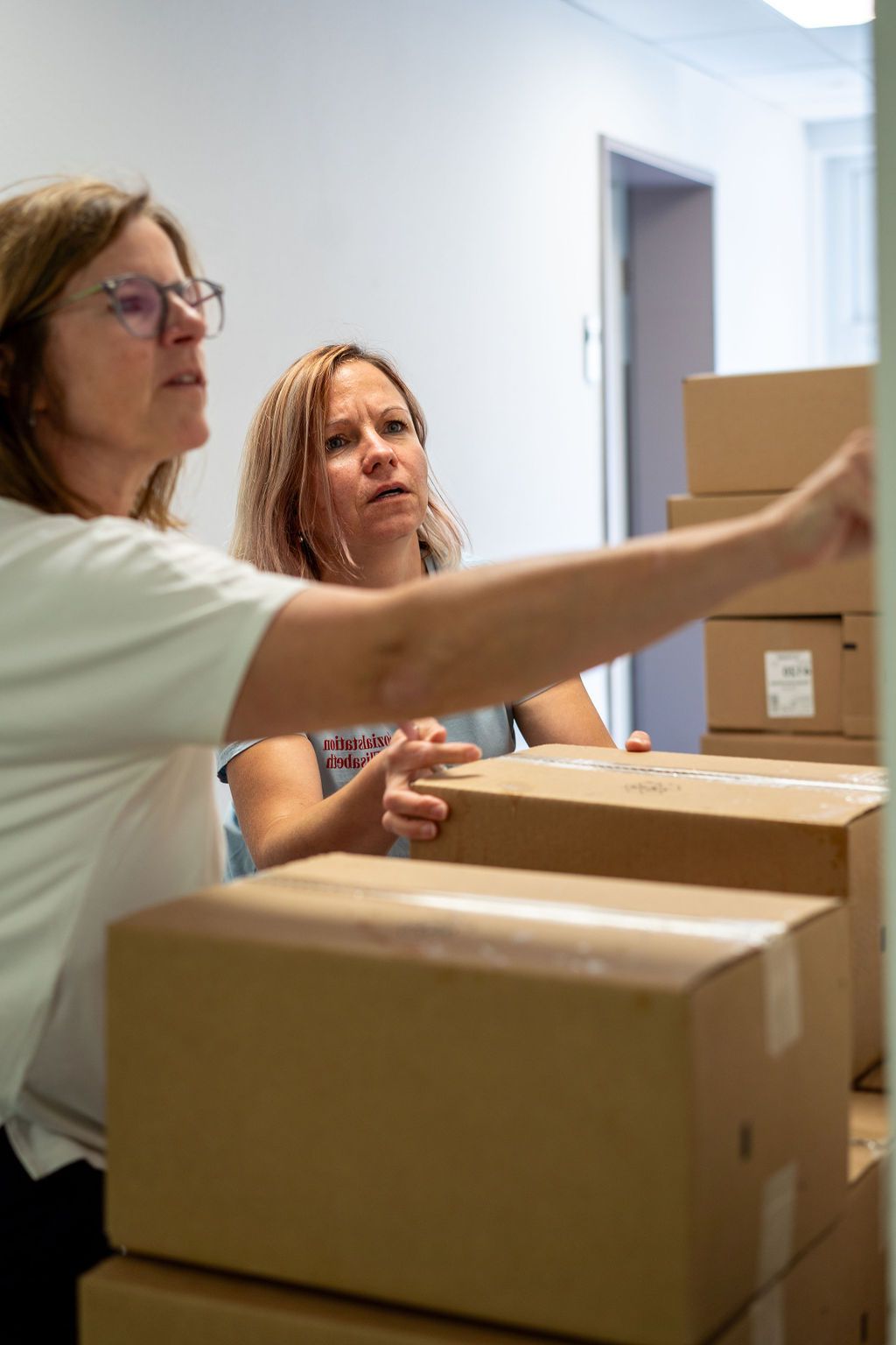 Zwei Frauen stehen nebeneinander vor einem Stapel Kartons.