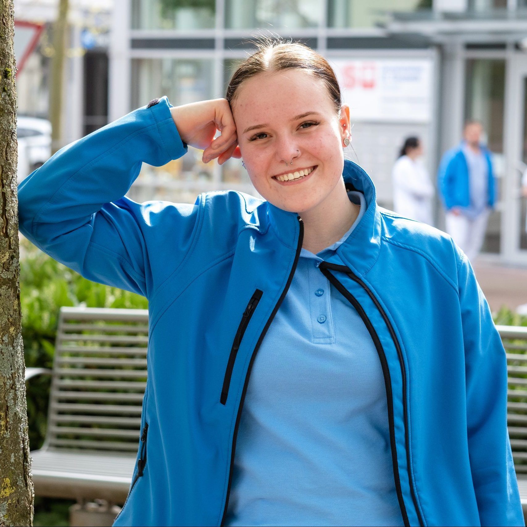 Mitarbeiterin der Katholischen Sozialstationen in Mittelbaden lehnt an einem Baum vor dem Betriebsgebäude.