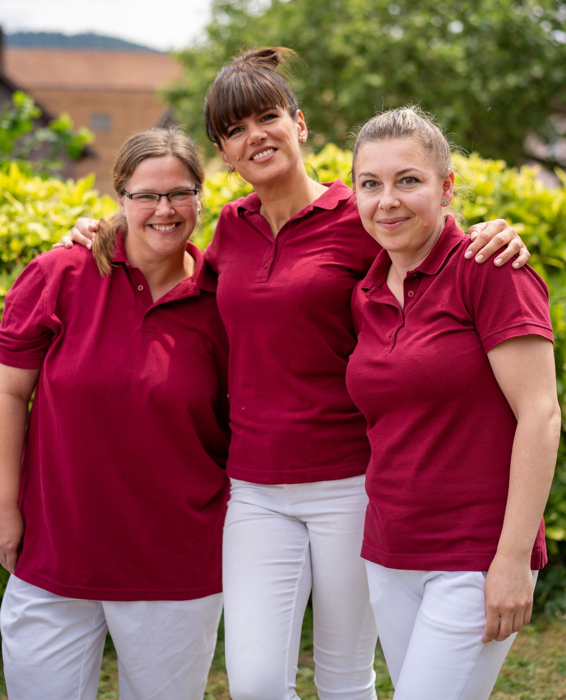 Drei Pflegefachkräfte in Arbeitskleidung Arm in Arm