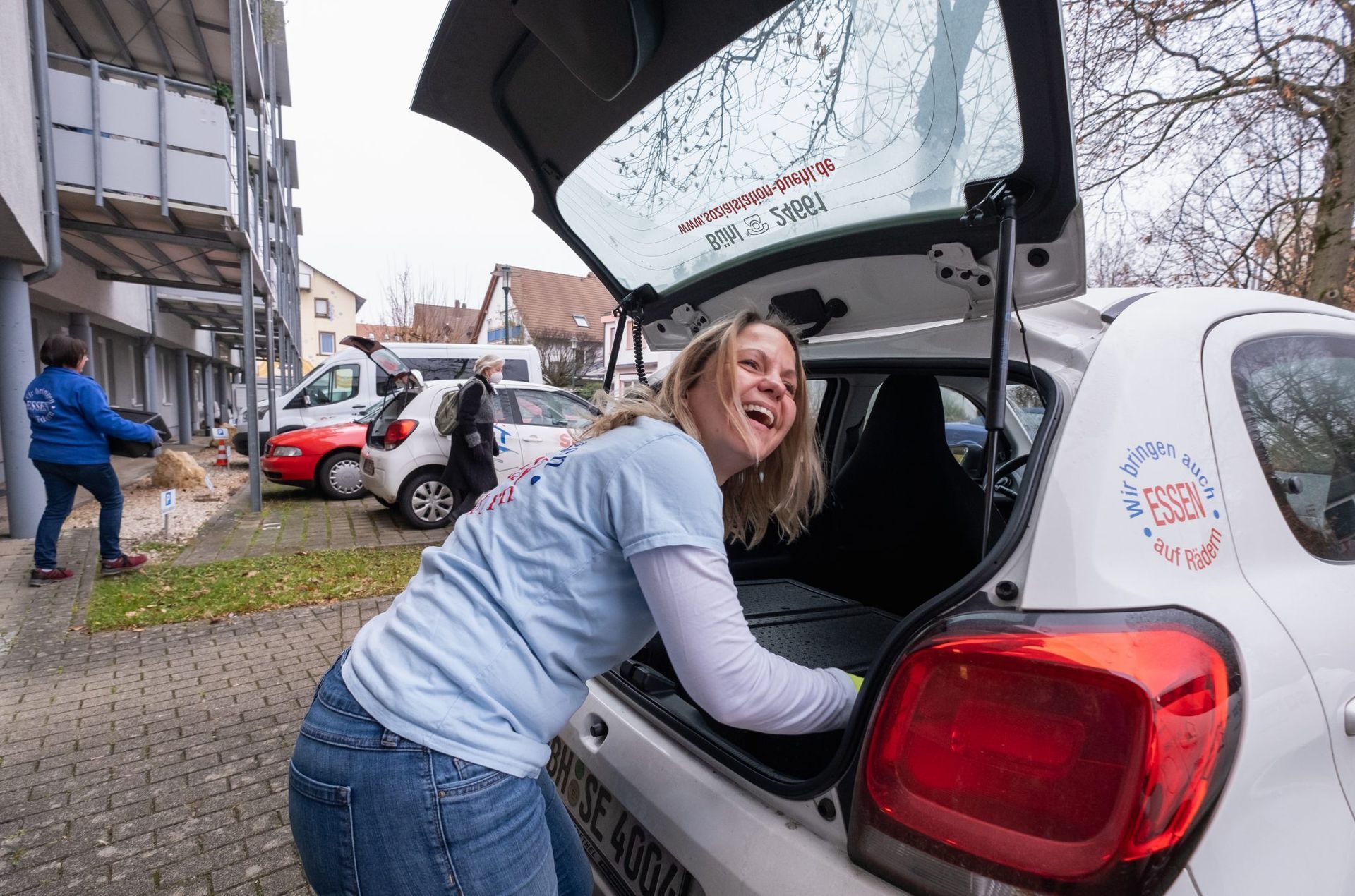 Mitarbeiterin belädt das Dienstauto mit den Boxen für Essen auf Rädern.