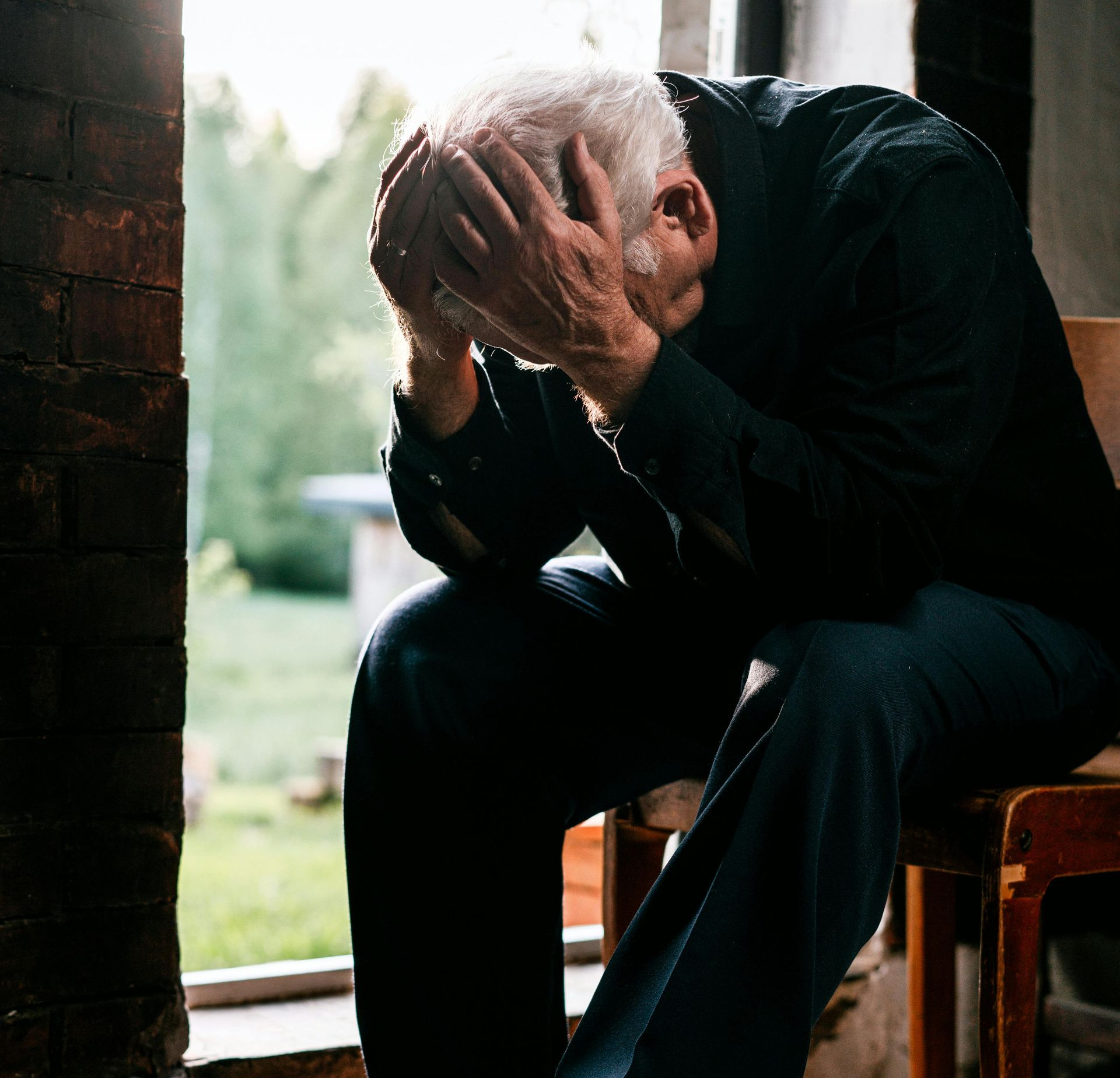 Älterer Mann vergräbt Gesicht in seinen Händen weil er depressiv ist