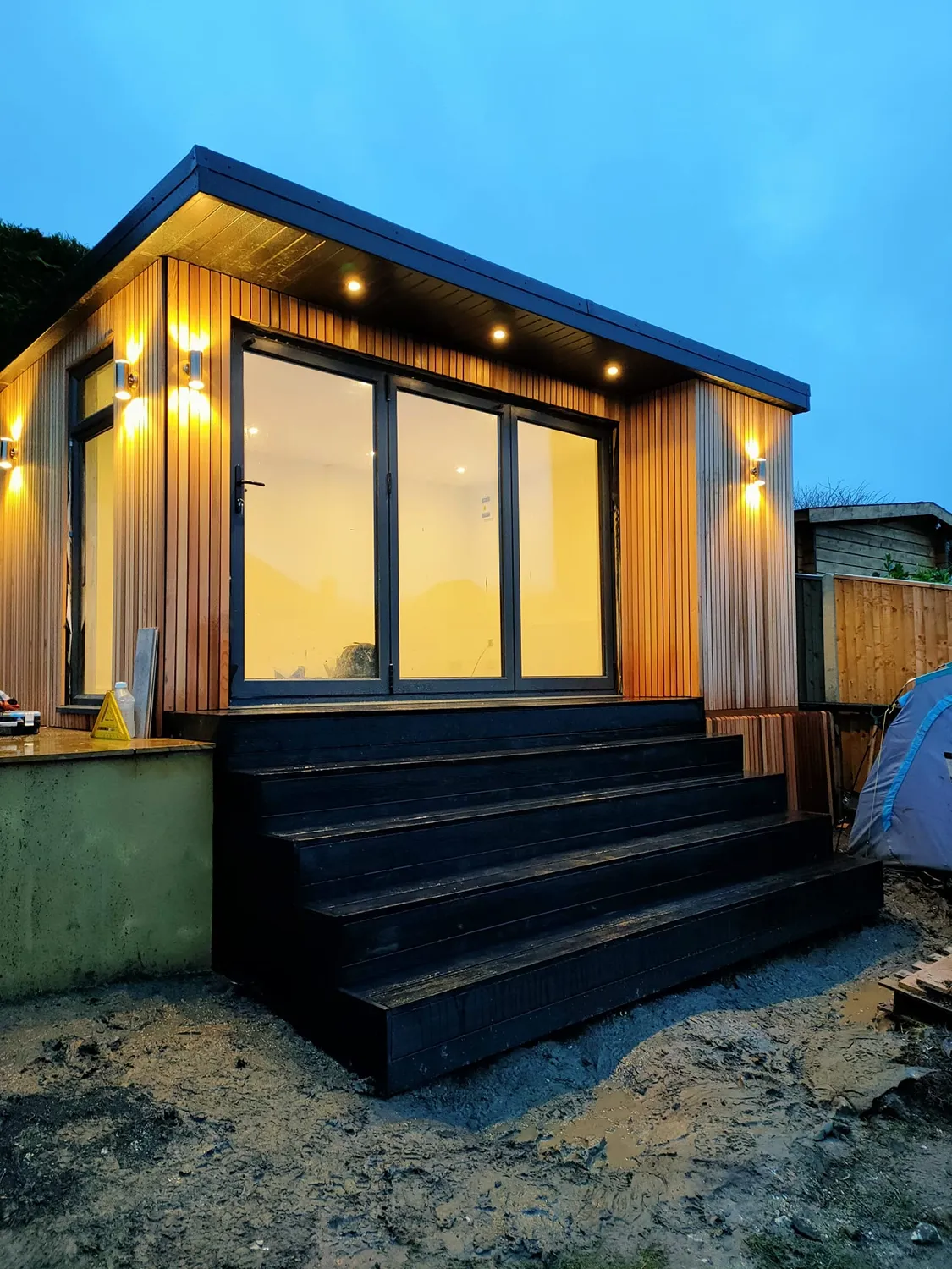 A Timber Garden Room with stairs leading up to it is lit up at night.