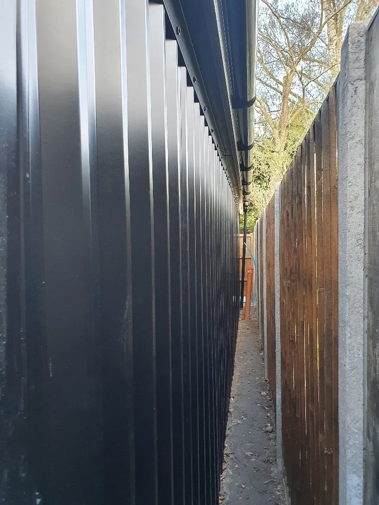 A narrow alleyway with a black wall and a wooden fence.