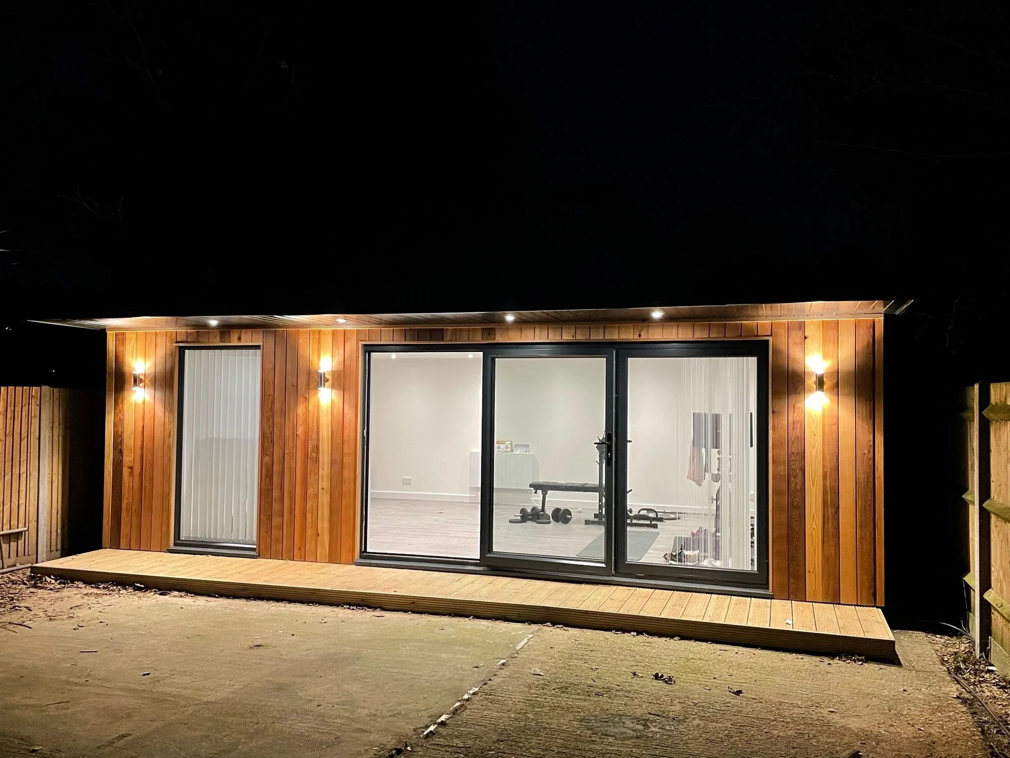 A Timber Garden Room with sliding glass doors is lit up at night.