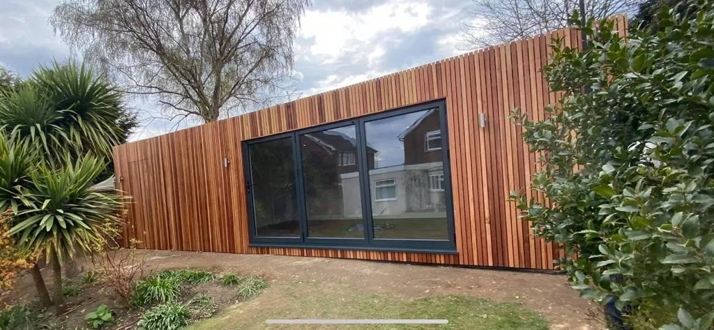 A Timber Garden building with a lot of windows and trees in the background.