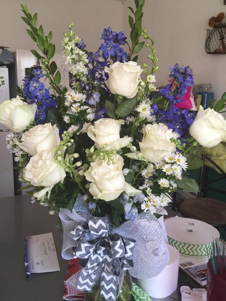 Bouquet of white roses and blue delphiniums with greenery, tied with a blue and gray ribbon.