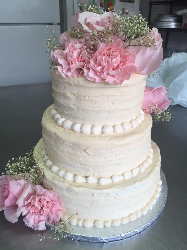 Three-tiered cake with cream frosting, pink flowers, and white beaded border on a silver tray.