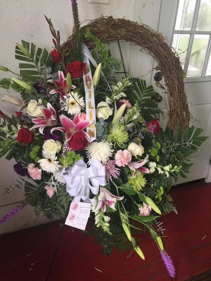 Floral wreath with red roses, lilies, and white bow.