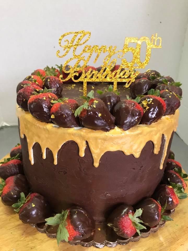 Chocolate cake with gold drip, topped with chocolate-covered strawberries and a