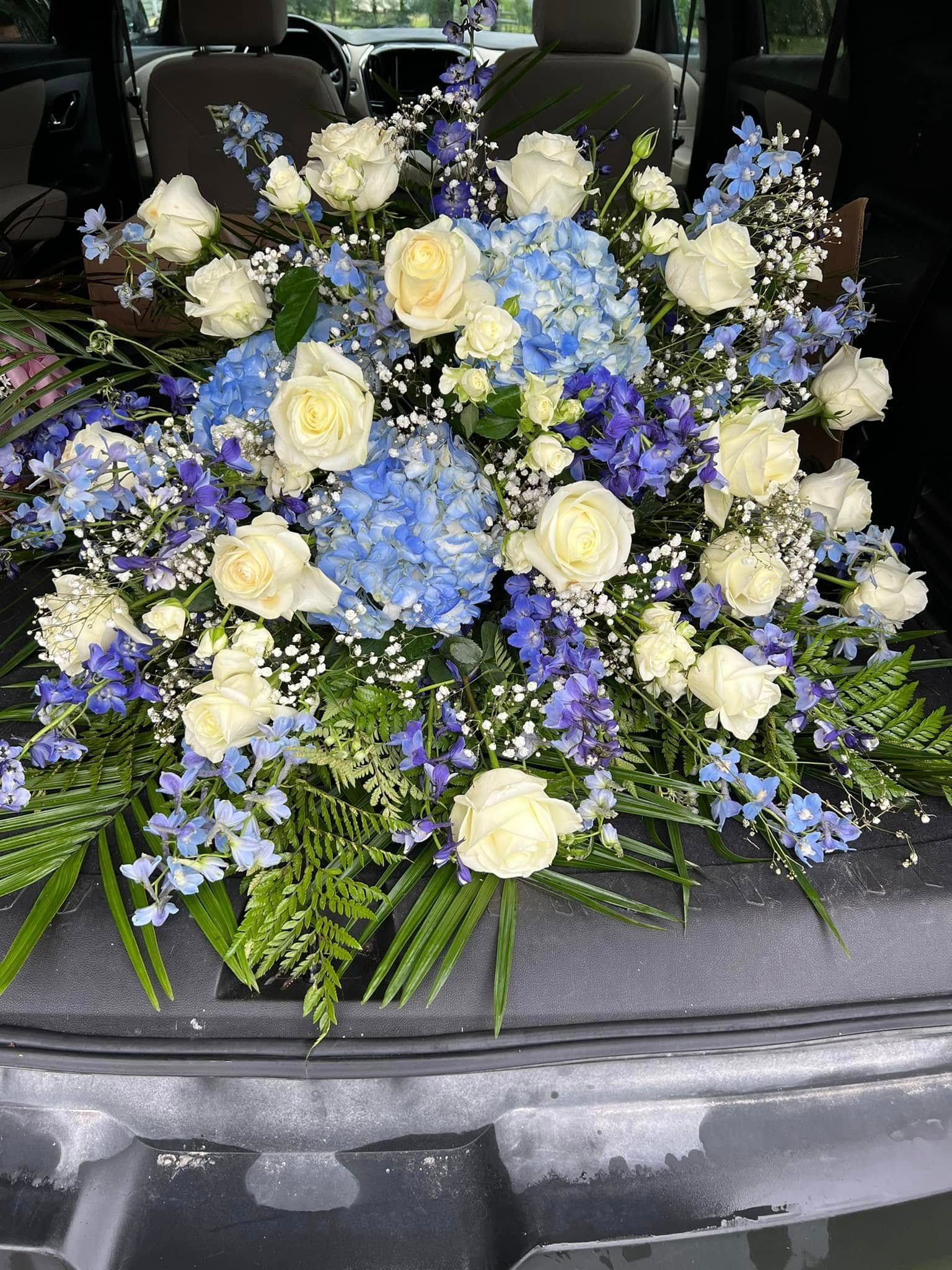 Floral arrangement with white roses, blue hydrangeas, and greenery.
