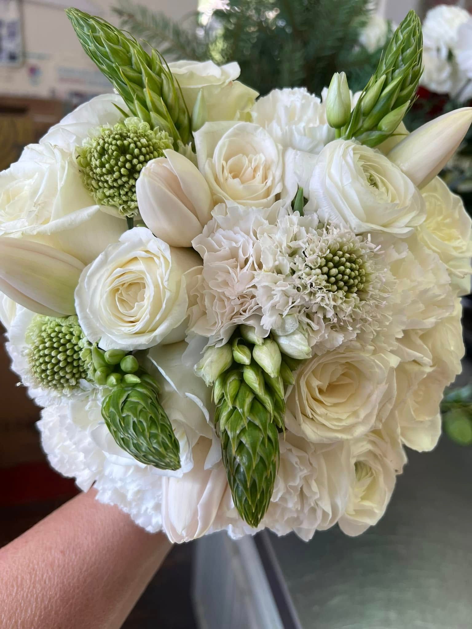 White and green floral bouquet held in hand, featuring roses, tulips, and other blooms.