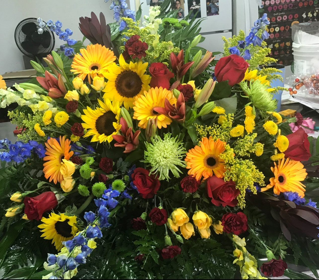 Colorful floral arrangement with sunflowers, gerbera daisies, roses, and greenery.