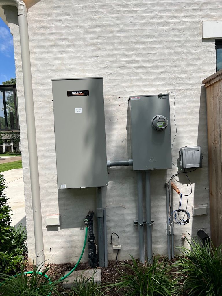 Gray electrical boxes mounted on a white brick wall, with a green hose and utility pipes.
