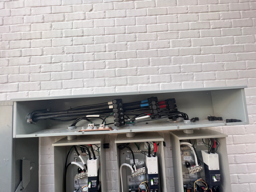 Electrical meters in gray boxes on a white brick wall. Wires and components visible.