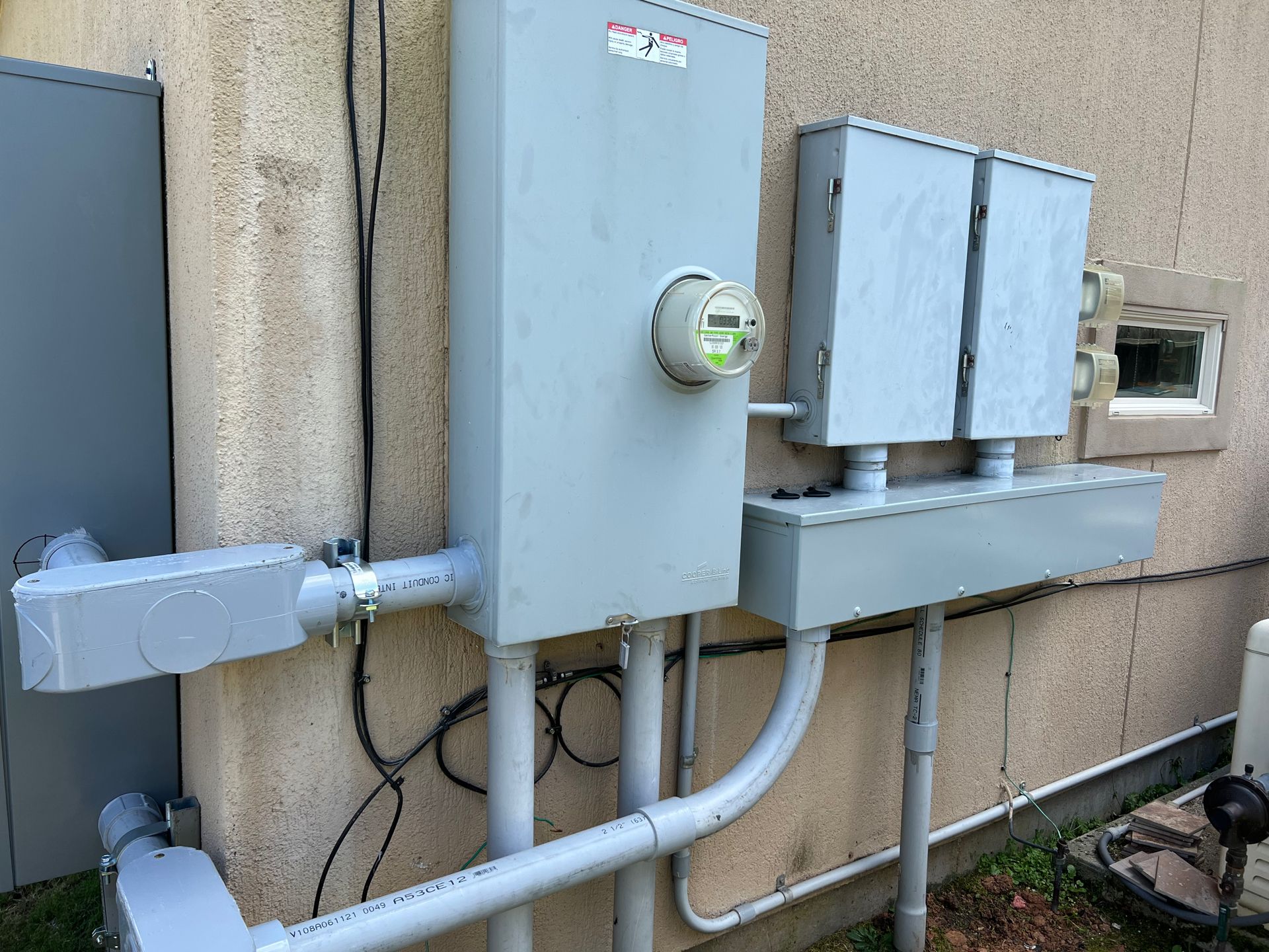 Exterior electrical panel on a stucco building with conduit and meter.