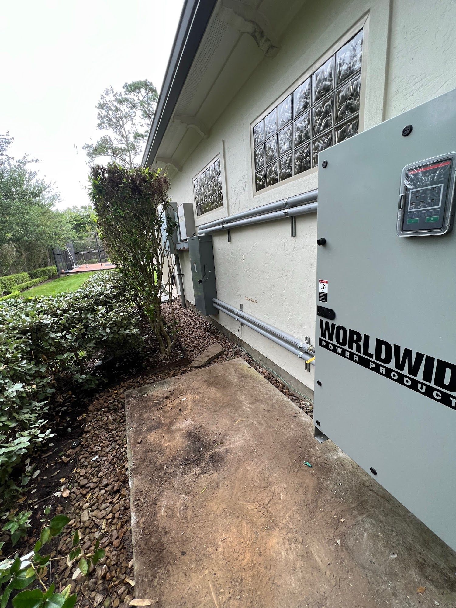Exterior of a building with electrical equipment and conduit along the wall next to a concrete walkway.