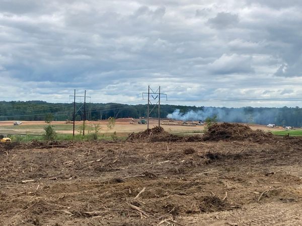 Construction site with smoke and power lines under a cloudy sky. Brown debris in foreground.