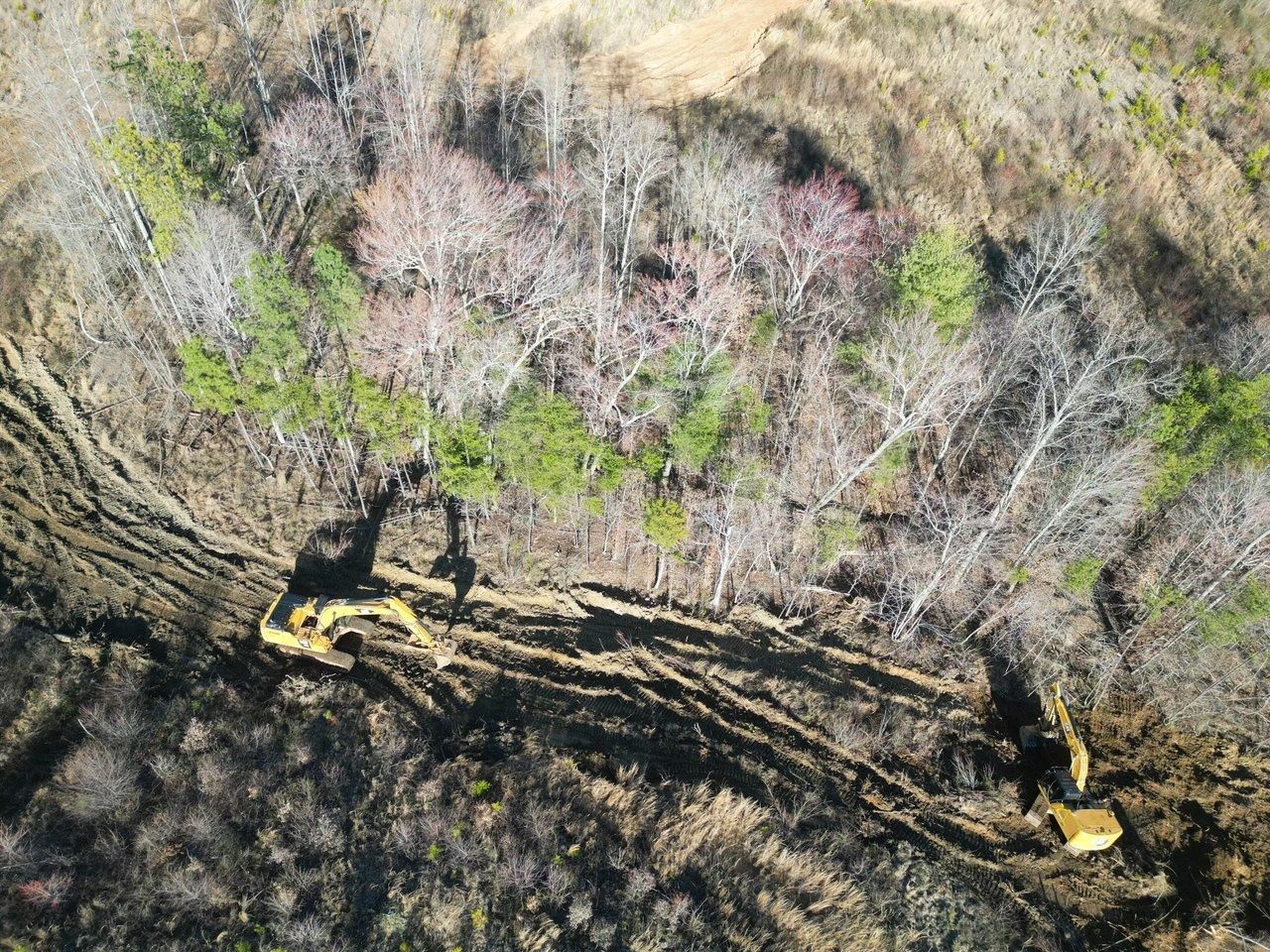Aerial view of construction in a wooded area with heavy machinery carving a path.