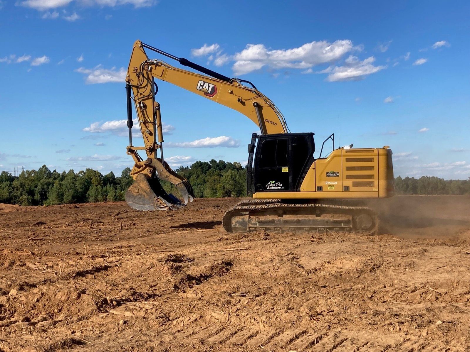 Yellow excavator working on a dirt field under a blue sky, clearing land.