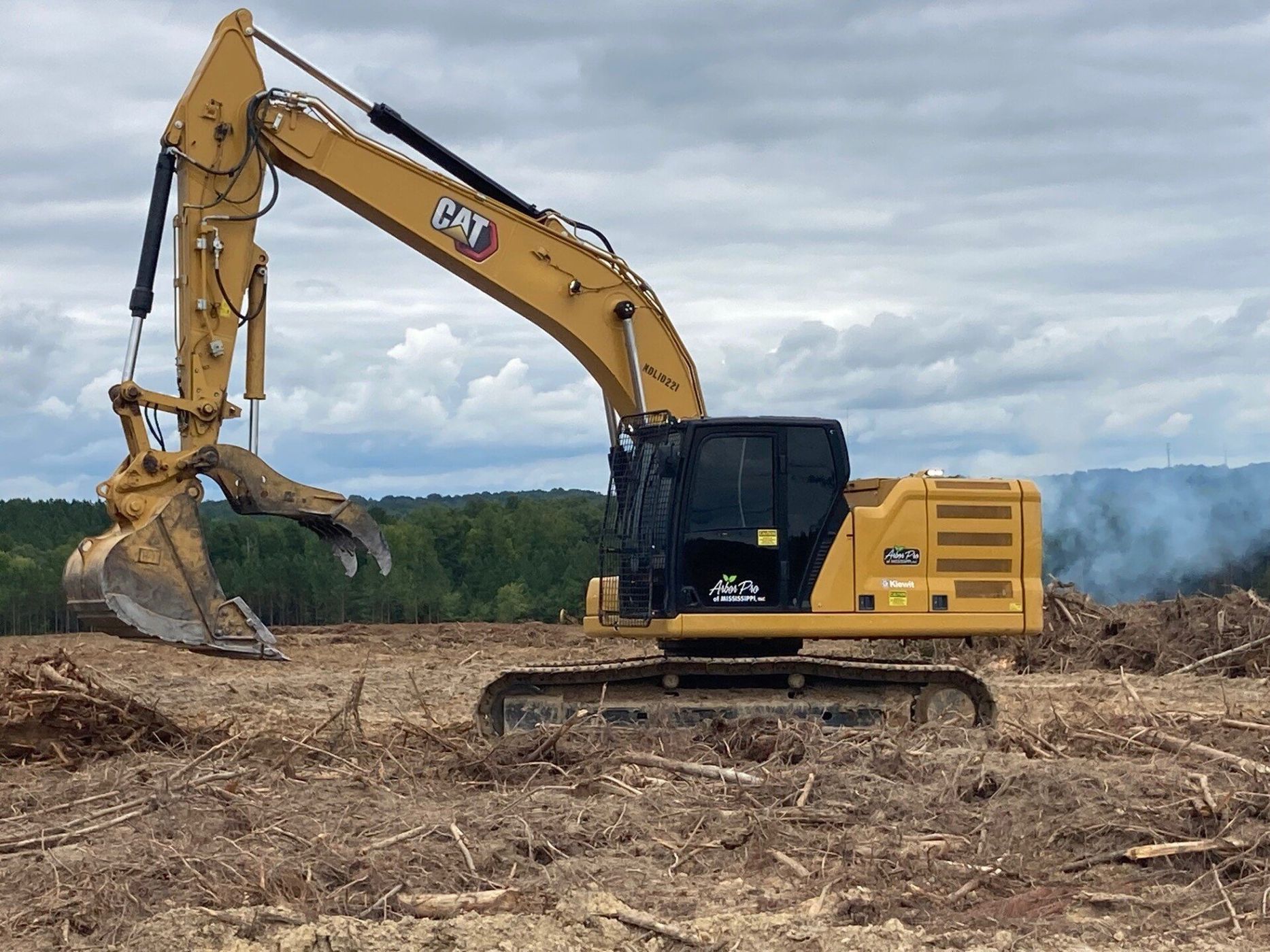 Yellow Caterpillar excavator clearing a field, smoke in background.