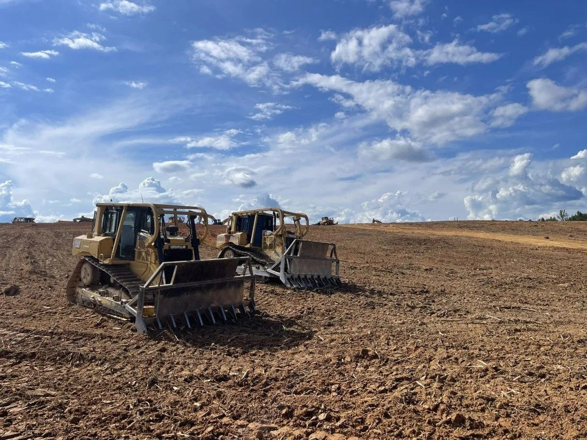 Two yellow bulldozers on a brown field under a partly cloudy blue sky.