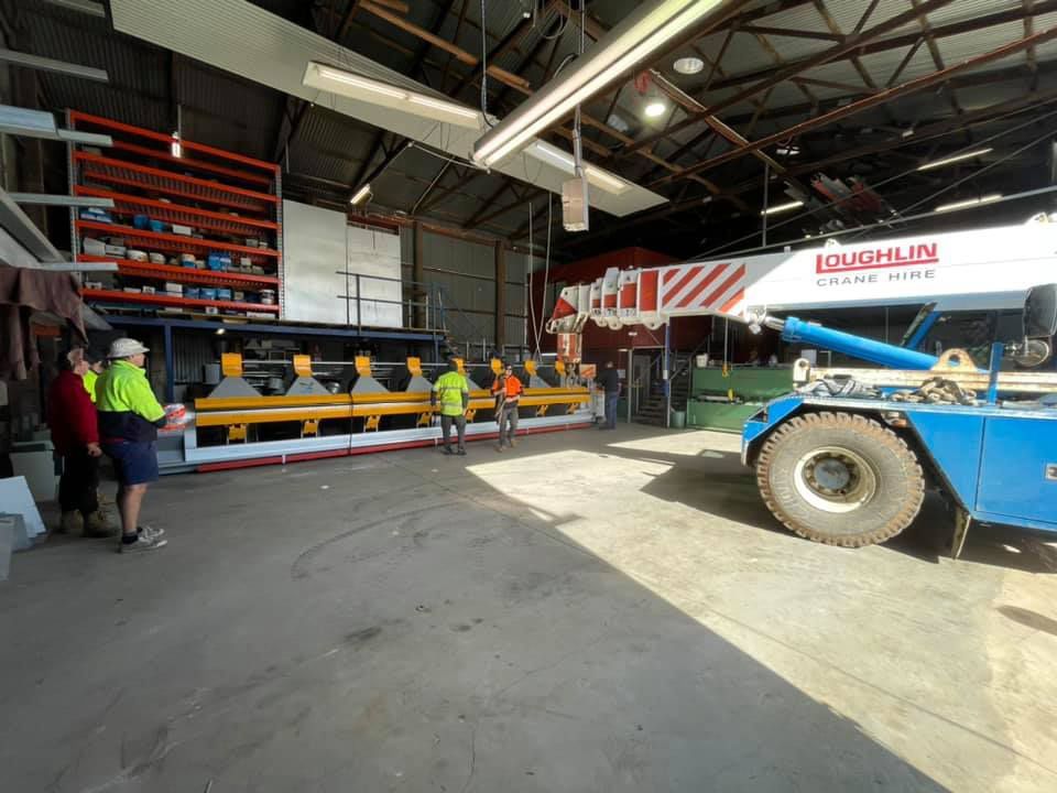 A Group Of People Are Standing Around A Crane In A Garage — Roofer in Toowoomba, QLD